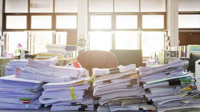 Paper records piling up on a desk to be filed using a records retention policy
