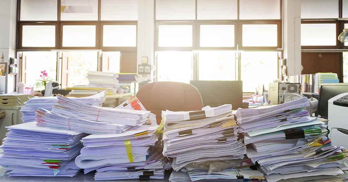 Paper records piling up on a desk to be filed using a records retention policy