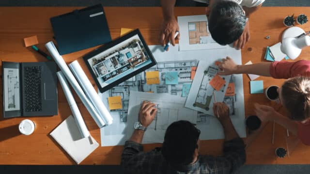 Top down view of civil engineer handed document while looking at blueprint. Aerial view of architect team brainstorming idea and planning building design while sitting at table with plan. Symposium.